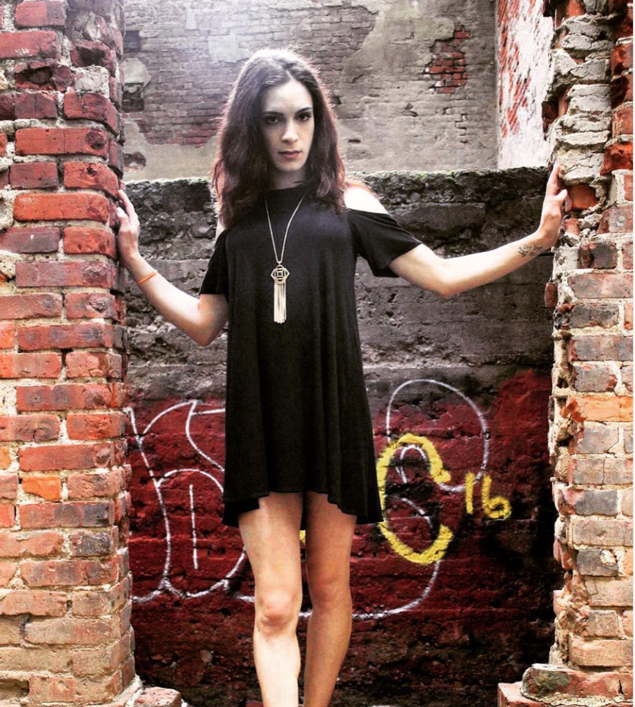 Arielle wearing a black dress, standing in a brick archway.